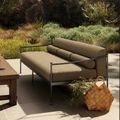 Outdoor patio lounge chair with metal frame and beige cushions, next to a wooden table and wicker basket on a stone patio.