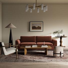 Modern living room with rust sofa, wooden chairs, coffee table, lamp, and wall art in a stylish interior setting.