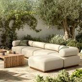 Modern outdoor sectional sofa on a patio with plush cushions and wooden coffee table, surrounded by greenery.