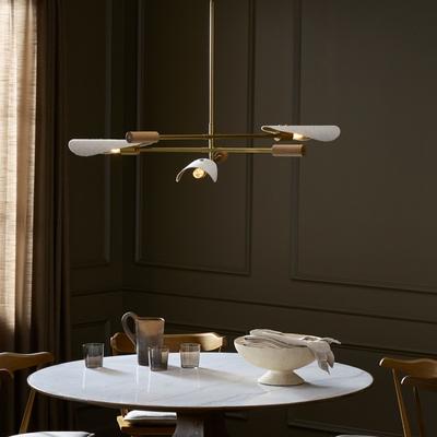Modern brass chandelier with white shades and LED bulb above a stylish dining table in an elegant room.