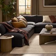 Modern living room with dark sectional sofa, plush cushions, wooden coffee table, elegant decor, and soft neutral tones.