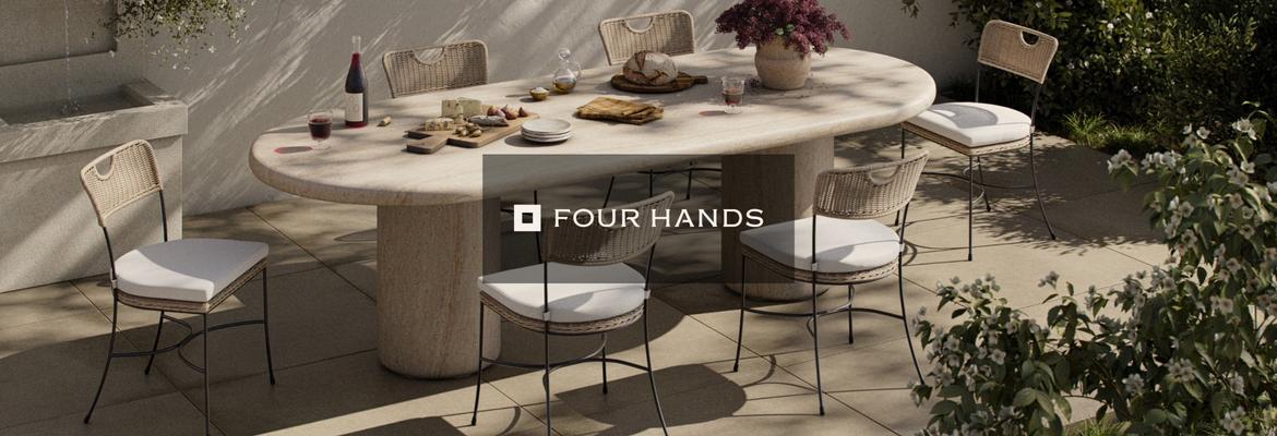 Modern outdoor dining set by Four Hands featuring a stone table and wicker chairs with cushions on a patio.