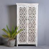 White wooden decorative wardrobe with intricate carved design, next to a potted plant in a grey interior setting.aaaaaaa